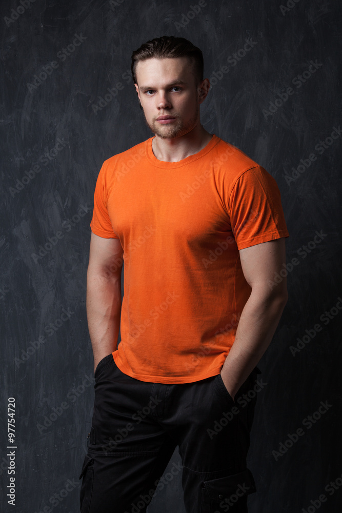 Strong man in an orange shirt tucked hands in his pockets Strong man in an orange shirt tucked hands in his pockets