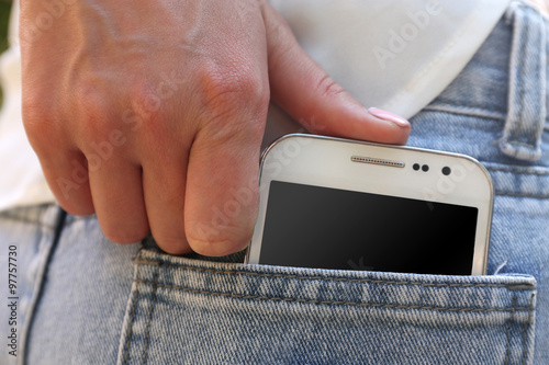 Female hand puts white smart mobile phone into jeans pocket