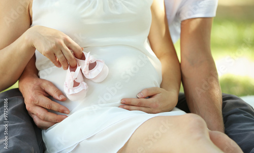 Handsome man and his lovely pregnant wife with baby booties in the park, close up