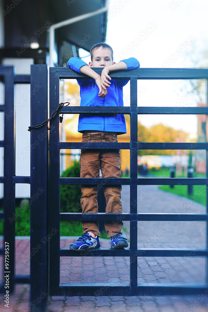 boy looking over the fence. boy stands on an iron fence at the house. sad sight. waiting for something or someone boy looking over the fence. boy stands on an iron fence at the house. sad sight. waiting for something or someone