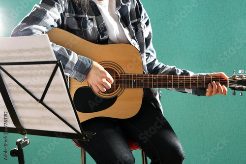 Musician plays guitar on blue background in studio with musical notes holder, close up