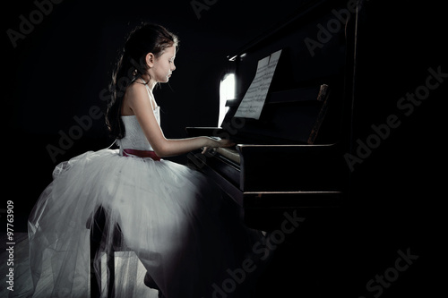 Cute little princess girl plays piano in the dark room photo