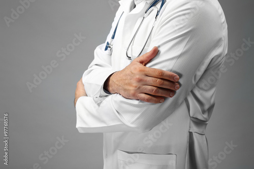 Doctor with crossed hands and stethoscope on grey background, close up