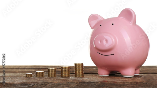 Piggy bank with coins on wooden table, isolated on white