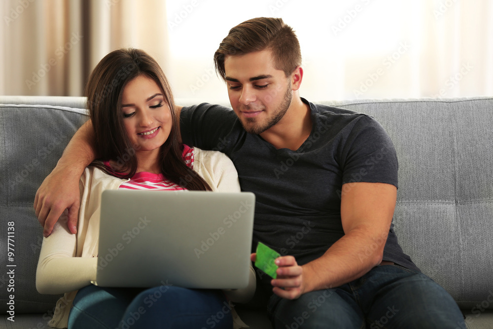 Young happy couple using credit card with laptop at home on light background Young happy couple using credit card with laptop at home on light background