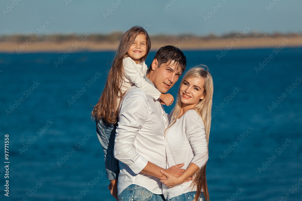 Young family in blue jeans hugging on the background of water