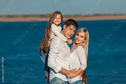 Young family in blue jeans hugging on the background of water © satyrenko