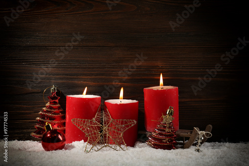 Three red candles, toys, star and sledge in a snow over wooden background, still life