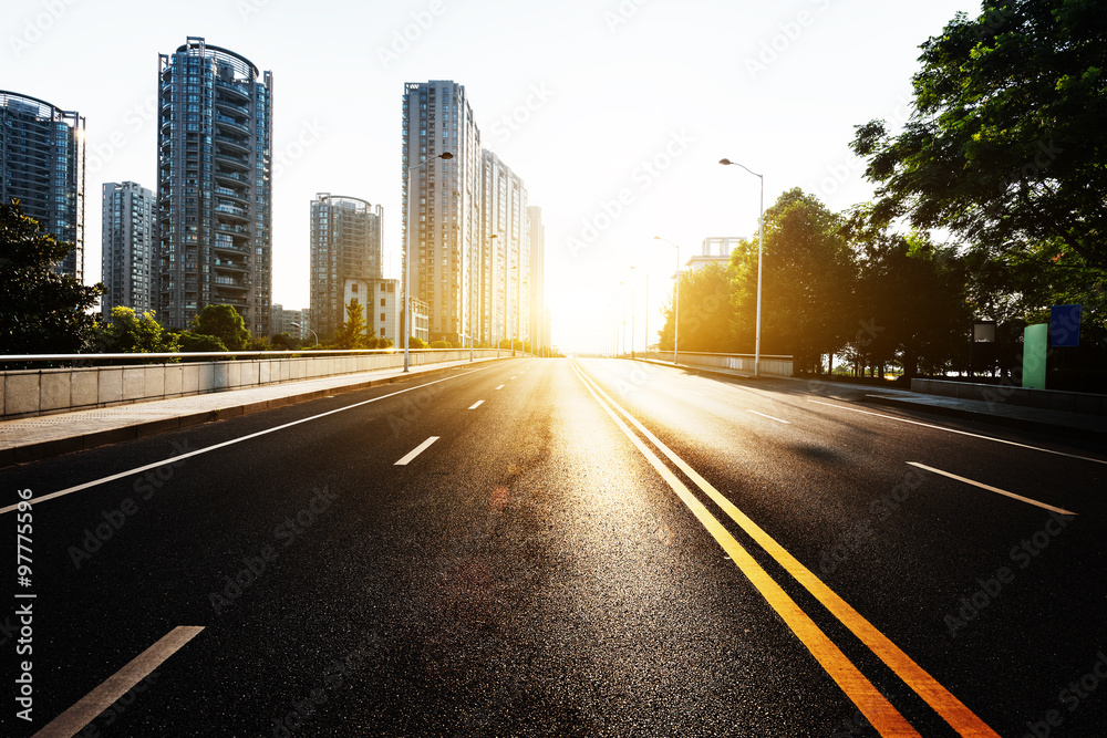sunlight,empty asphalt road by modern buildings