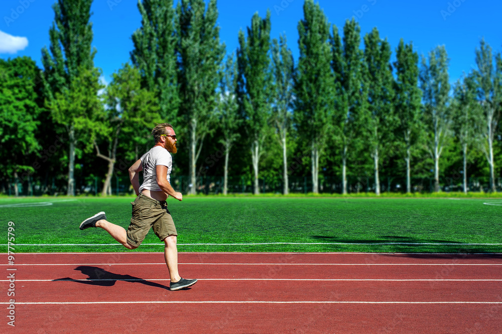 Bearded man running at stadium wearing sunglasses. Concept of persistence, healthy activity, goals achieving