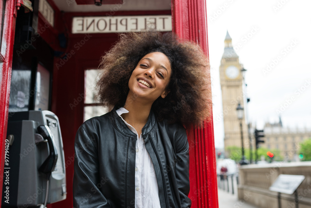 Naklejka premium Smiling portrait of young woman close to red telephone box in London.