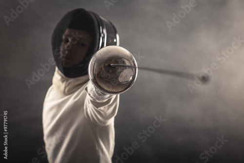 Boy wearing white fencing costume and black fencing mask standing with the sword practicing in fencing.  photo