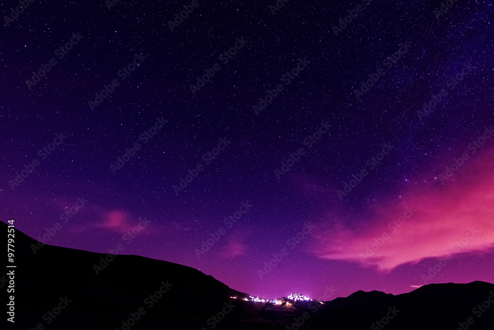Night stars over Castelluccio village and Sibillini mountains in Italy.