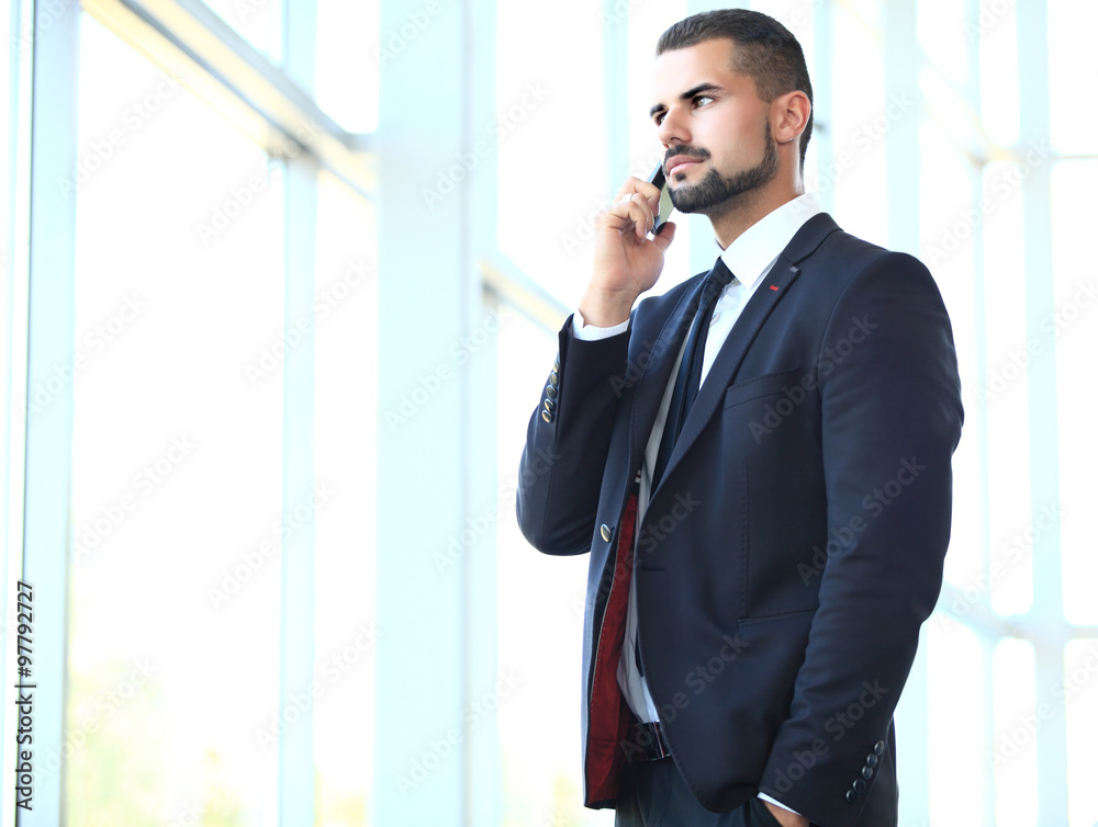 Portrait of a cheerful smiling men office worker talking on mobile phone while standing in modern office space, happy male entrepreneur having cell telephone conversation while resting after meeting Portrait of a cheerful smiling men office worker talking on mobile phone while standing in modern office space, happy male entrepreneur having cell telephone conversation while resting after meeting