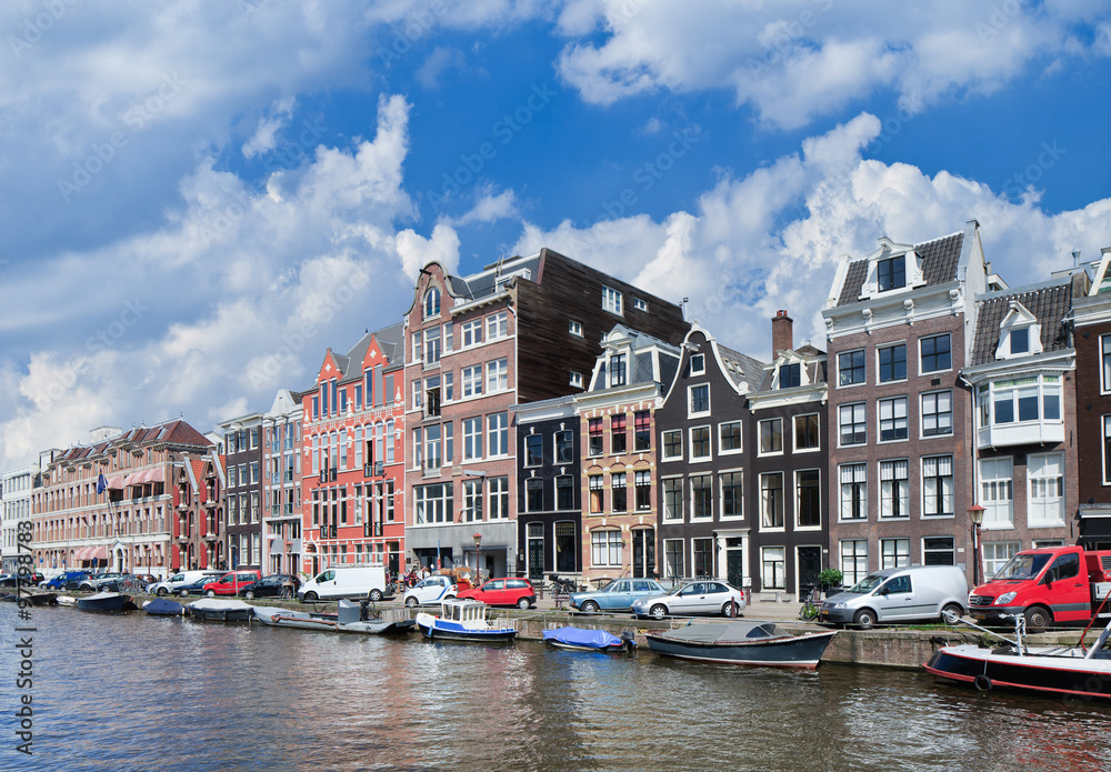 Canal with row of stately ancient mansions with parked cars and moored boats, Amsterdam, The Netherlands.