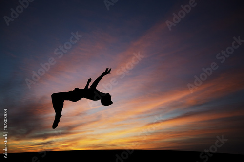 silhouetted gymnast doing backflip in sunset sky