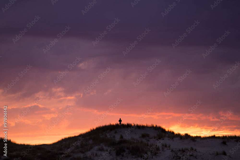 silhouetted boy on sand dune on French coast at sunset