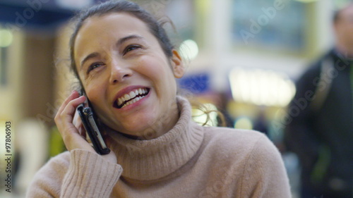  cheerful young woman talking on smart phone in busy train station or airpor photo