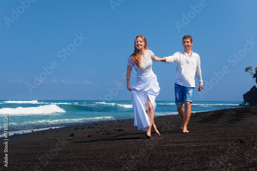 Happy newlywed family on honeymoon holidays - just married loving couple run with fun on sea black sand beach. Active lifestyle, people wedding outdoor activity on summer vacation on tropical island.