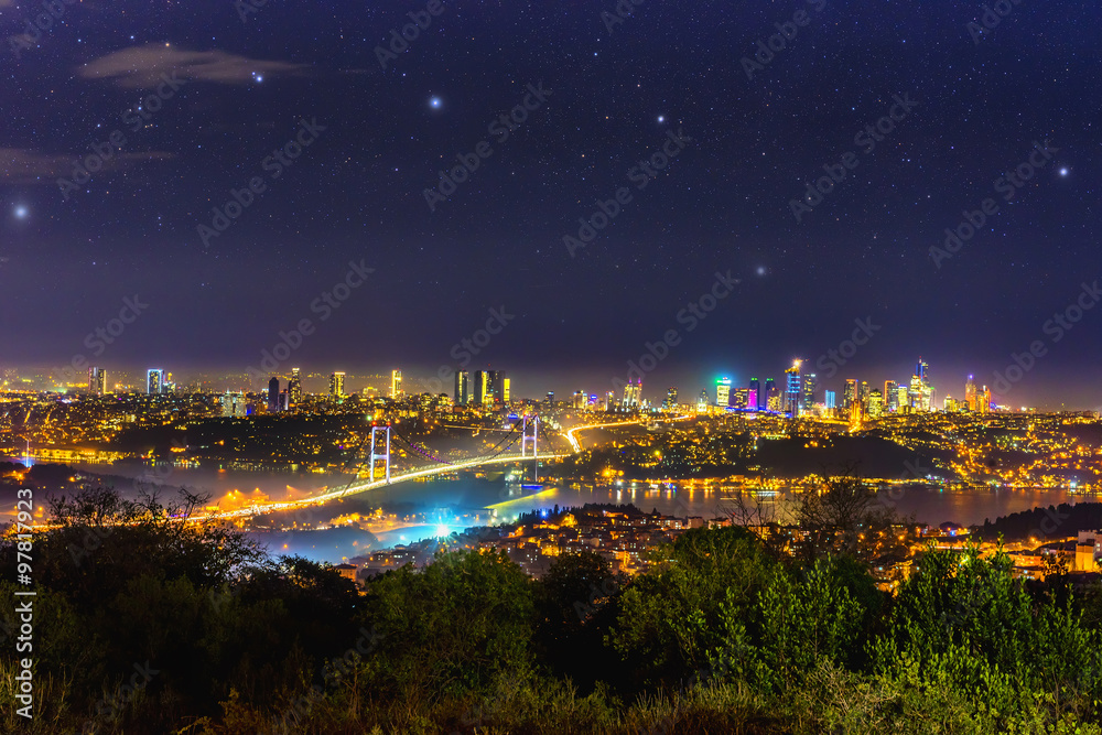 Istanbul, Turkey at night photographed from above in late November.  Costal line, a bridge  surrounded by residential buildings connecting  Bosphorus view followed by a distant Asian Sea shore.
