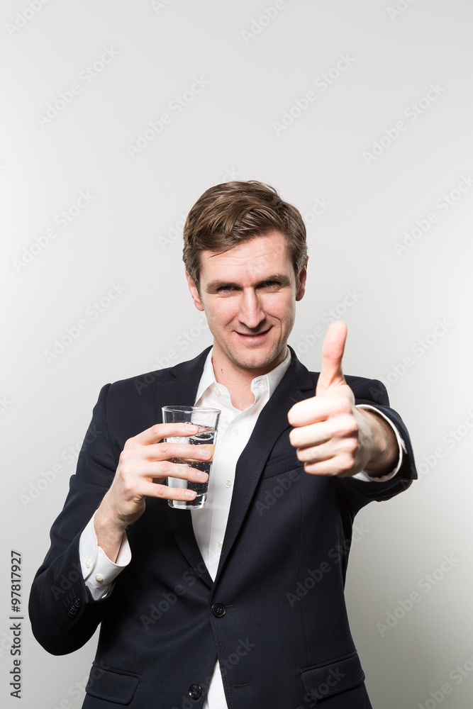 Blond-haired european businessman holding a glas of sparkling water and gives a thumps up directly to the camera in front of a gradient background Blond-haired european businessman holding a glas of sparkling water and gives a thumps up directly to the camera in front of a gradient background