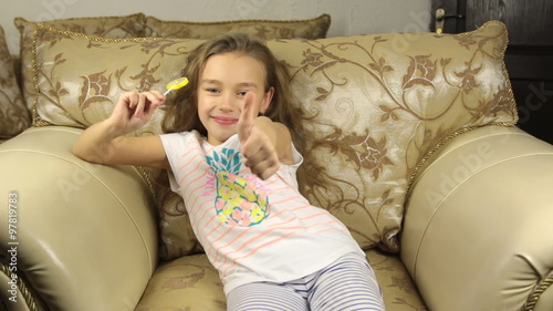 Girl licking candy on a stick in the form of lemon and raises the thumbs up