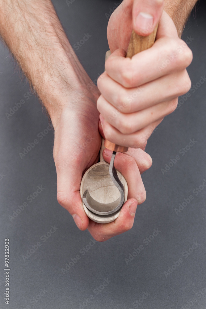 Fototapeta premium Man hands carving of a wooden spoon with hook knife on gray background