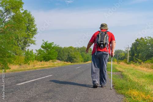 Elderly hiker walking on a roadside in Ukrainian rural area at summer time