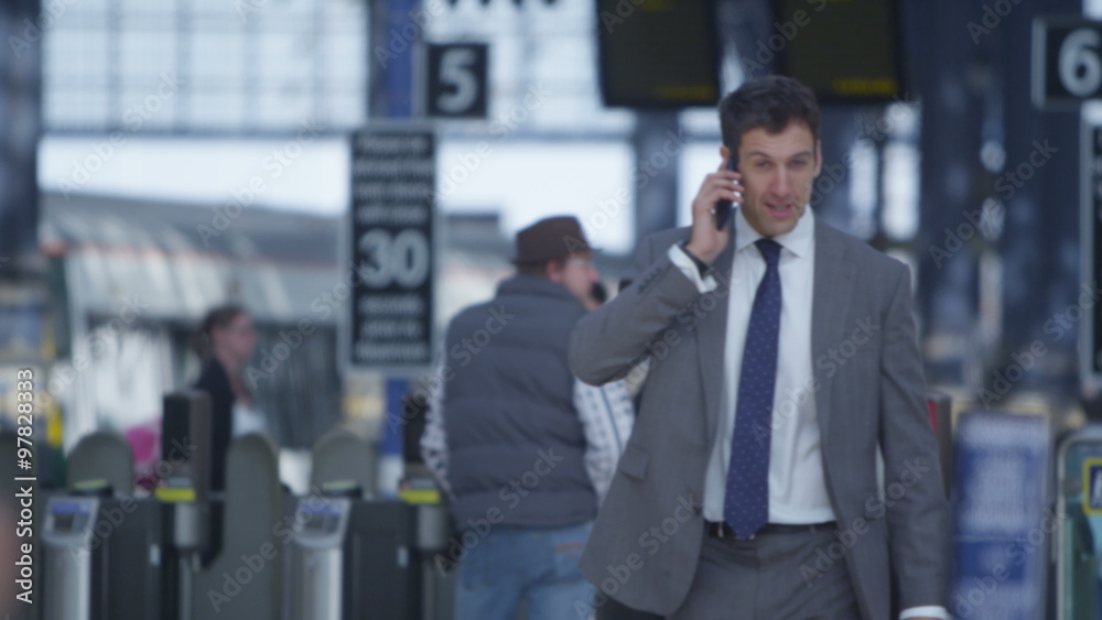 Attractive smiling businessman talking on phone as he walks through train station. Shot on RED Epic. Attractive smiling businessman talking on phone as he walks through train station. Shot on RED Epic.