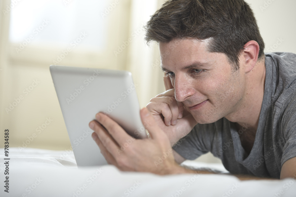 young attractive man lying on bed or couch enjoying social networking using digital tablet computer internet at home