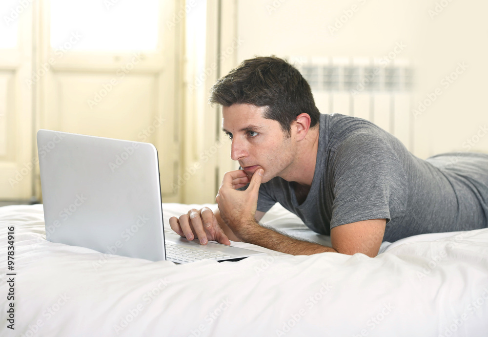 young attractive man lying on bed or couch working on computer laptop typing connected to internet young attractive man lying on bed or couch working on computer laptop typing connected to internet