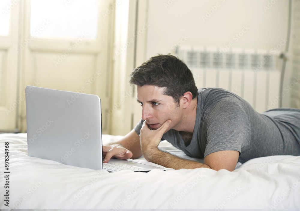 young attractive man lying on bed or couch enjoying social networking using computer laptop at home wireless internet young attractive man lying on bed or couch enjoying social networking using computer laptop at home wireless internet