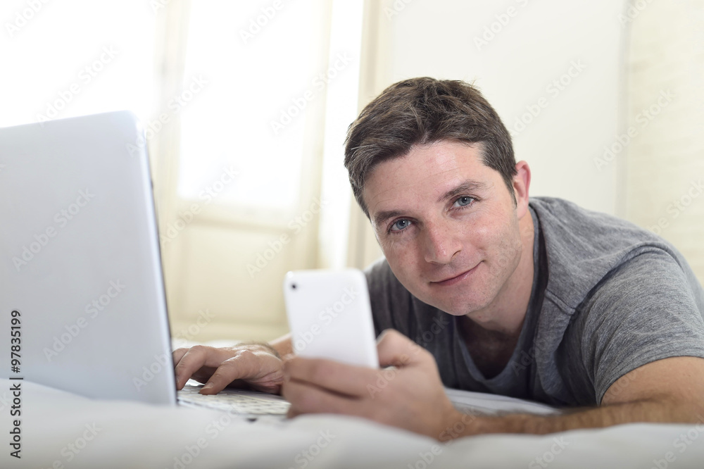 young attractive man lying on bed or couch using mobile phone and computer laptop internet addict