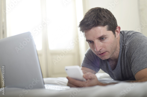 young attractive man lying on bed or couch using mobile phone and computer laptop internet addict