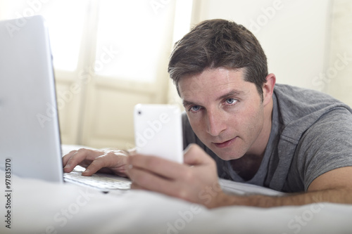 young attractive man lying on bed or couch using mobile phone and computer laptop internet addict © Wordley Calvo Stock