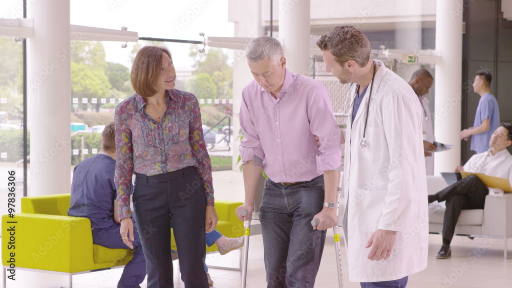 Caring doctor assisting patient walking with crutches in busy modern hospital Caring doctor assisting patient walking with crutches in busy modern hospital