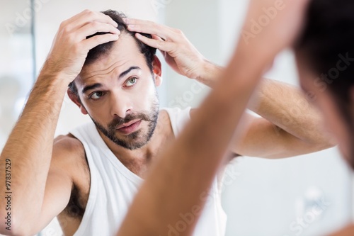 Concentrated man looking at his hair in mirror photo