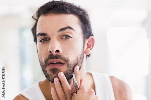 Concentrated man cutting his beard with scissors