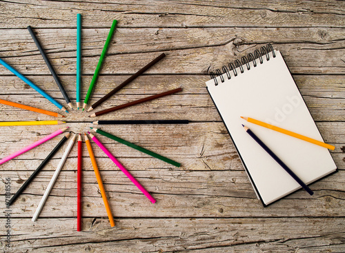 Colorful pencil crayons and notebook on wooden background