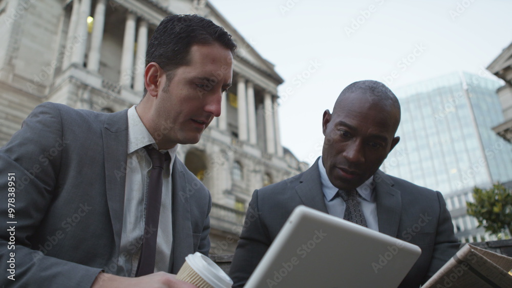 2 Businessmen working on wireless devices on a London street in the evening 2 Businessmen working on wireless devices on a London street in the evening