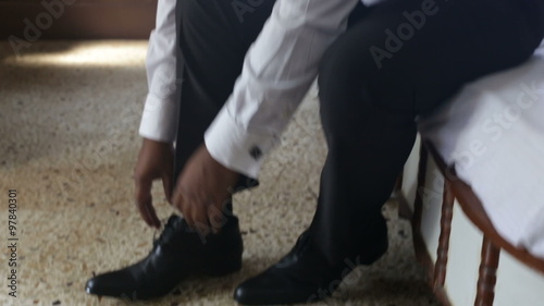 man in white wedding shirt puts on black shoes ties shoe-laces