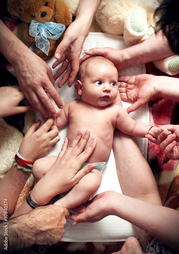 Newborn baby with big eyes being touched by hands of many family members. Symbol for love, care, protection, happiness.