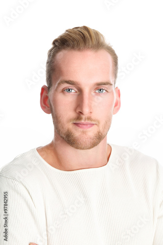 An attractive man in his 20s wearing a white sweater standing against a white background smiling against camera.