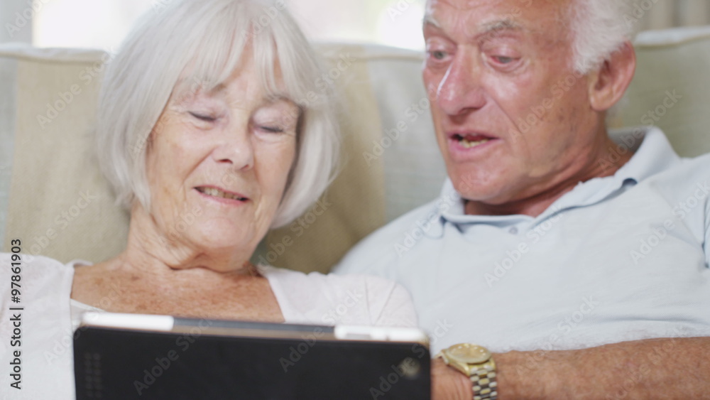 Cheerful senior couple relaxing at home with a computer tablet Cheerful senior couple relaxing at home with a computer tablet