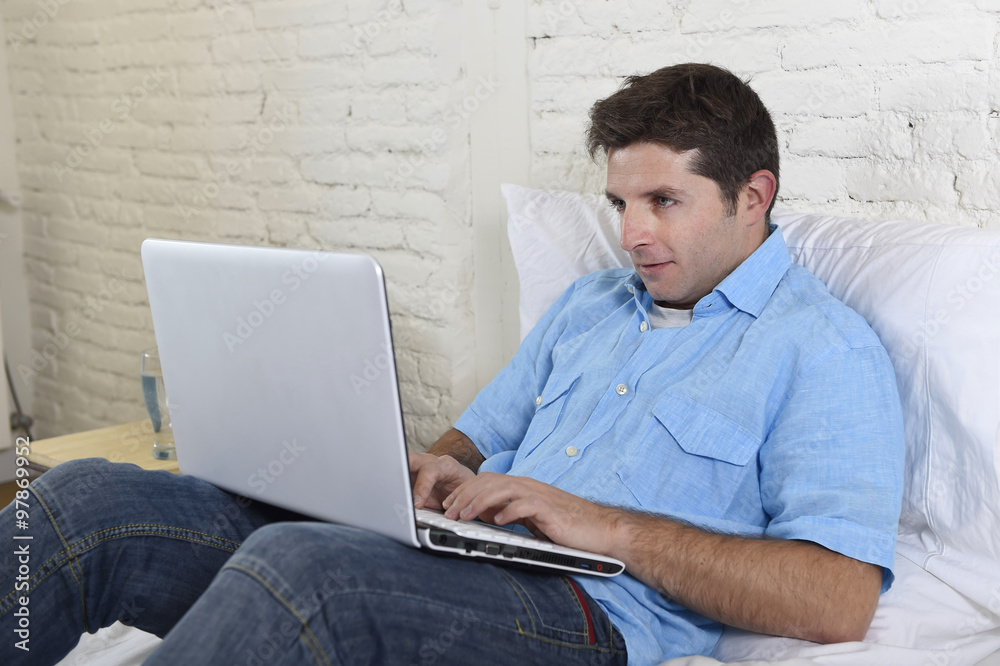 young attractive man lying on bed enjoying social networking using computer laptop at home
