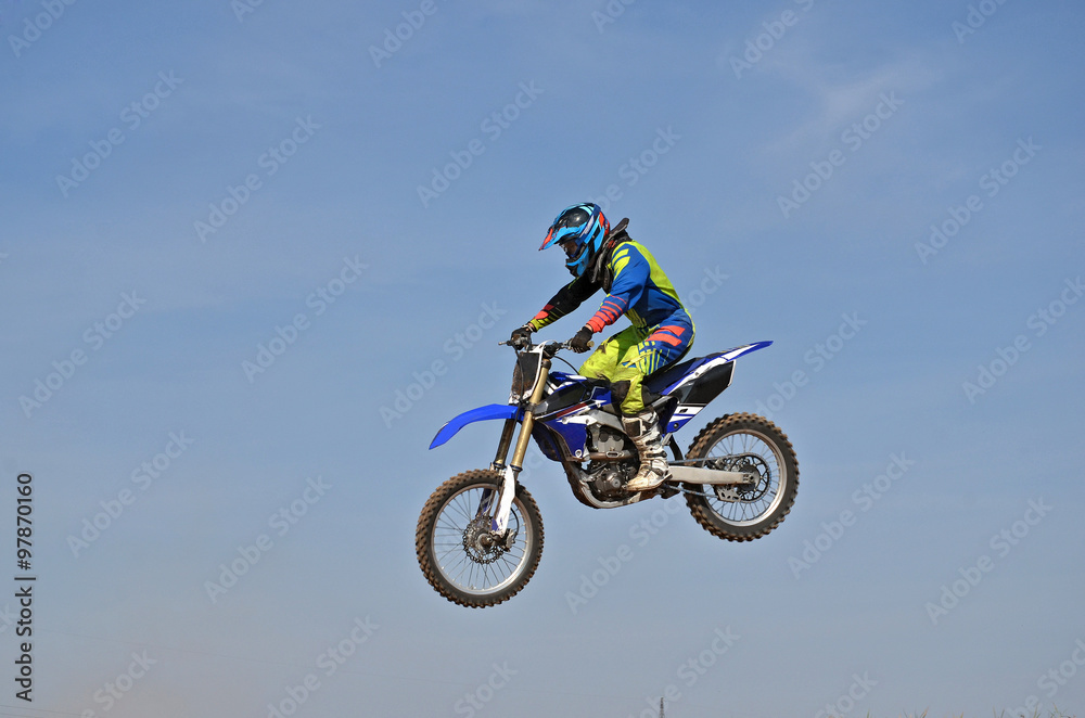 Motocross rider flying high on against a blue sky in the air separately Motocross rider flying high on against a blue sky in the air separately