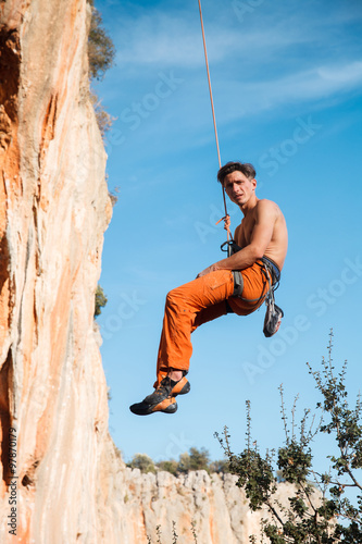 Rock climber hanging on belay rope over the mountains