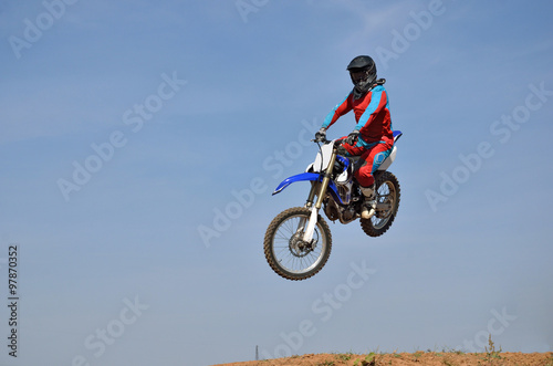 Motocross rider performs a jump on a motorcycle sideways looking at the camera  against a blue sky