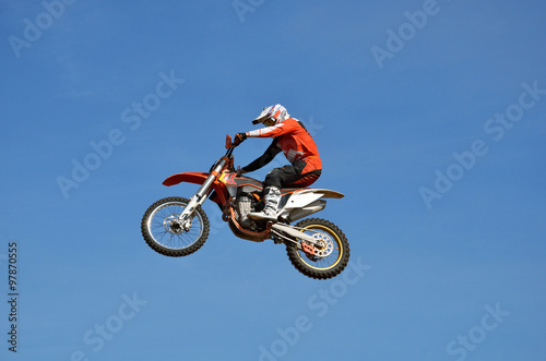 Freestyle tall flight on the MX bike athlete in the the form of an orange, on the background of the clear blue sky 