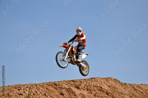 MX rider on a motorbike jumps down the slope turning his head looking at the camera